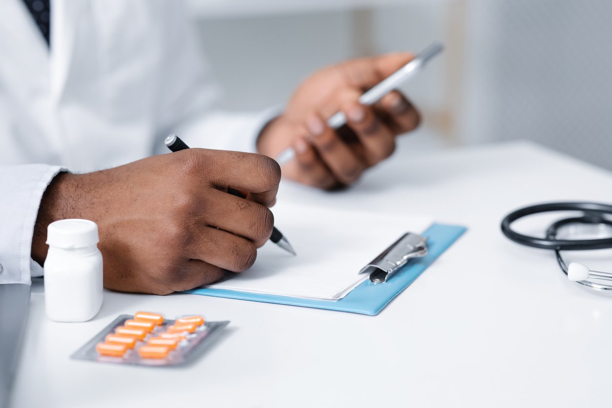 Cropped of black doctor making pills prescription online, using mobile phone, filling medical chart